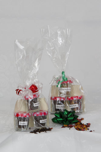 Photo shows two sets of a trio of teas in small jars with red and white lids. Each jar contains loose leaf tea in different flavours. One set contains all black loose leaf teas. The other set contain different loose fruit herbal teas. The packages are wrapped in clear cellophane and decorated in red and white or green and white curling ribbon. A festive Christmas gift for tea lovers.