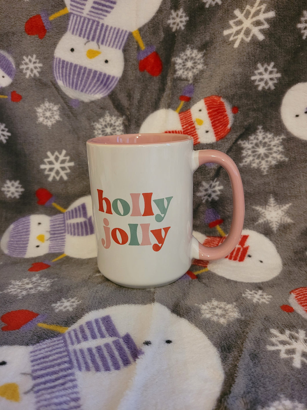 White mug with pink handle and pink interior of mug. Mug has the words holly jolly written on the front and back in the colours red, green and pink.  A great big mug to enjoy your Christmas tea in!